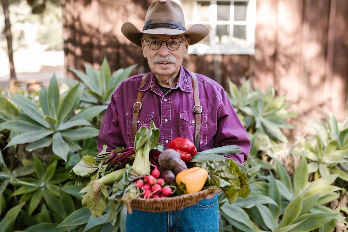 A grower holding a basket of fresh vegetables in a garden