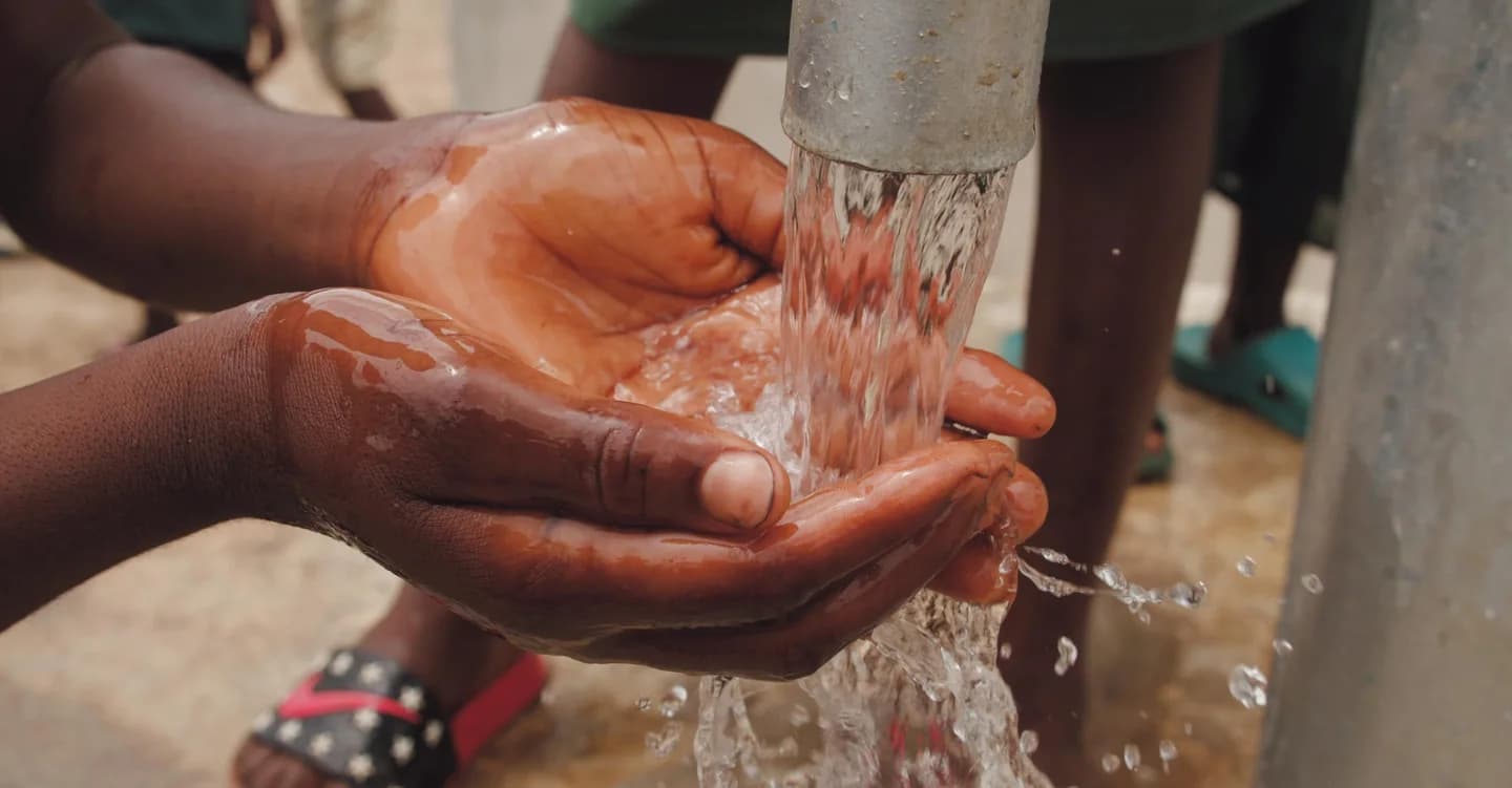 Hands catching flowing water from a pump