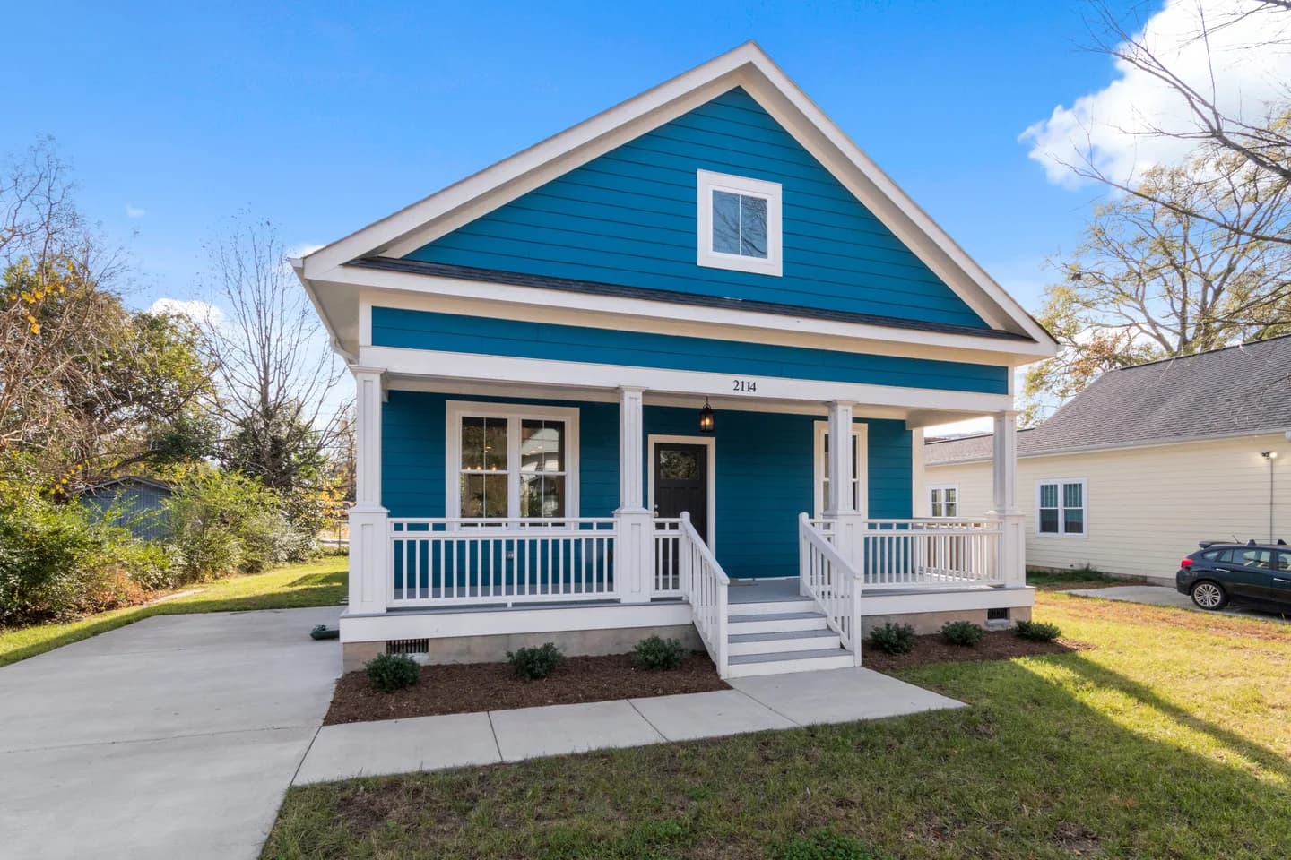 A modest blue house with a front porch and lawn